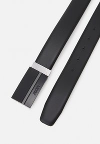 Cinturón de cuero negro con una hebilla rectangular plateada brillante. La hebilla presenta un acento texturizado y tiene múltiples agujeros de ajuste en la correa.