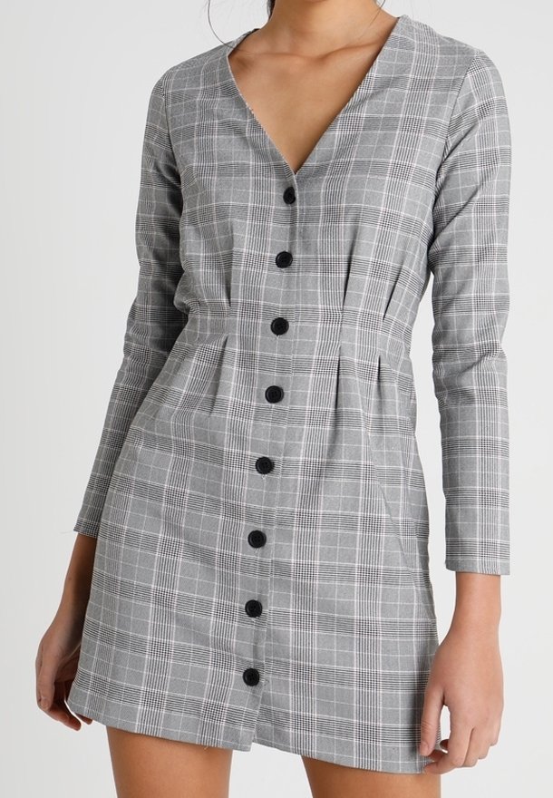 Robe à carreaux grise à manches longues, avec un col en V, des boutons sur le devant, un design plissé et des boutons noirs. Fabriquée en tissu texturé.
