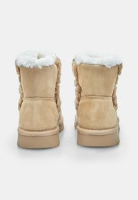 Pár béžových semišových zimných topánok s bielym chlpatým podšívkou, zobrazených zozadu na čistom bielom pozadí.