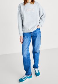 Sudadera de algodón gris con el logotipo bordado de "Levi's", combinada con jeans de mezclilla azul claro y zapatillas en color teal con acentos blancos.