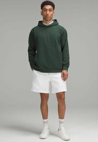 Groene katoenen hoodie met een kangoeroezak, gecombineerd met witte shorts en witte sneakers. De stof lijkt zacht en casual te zijn.