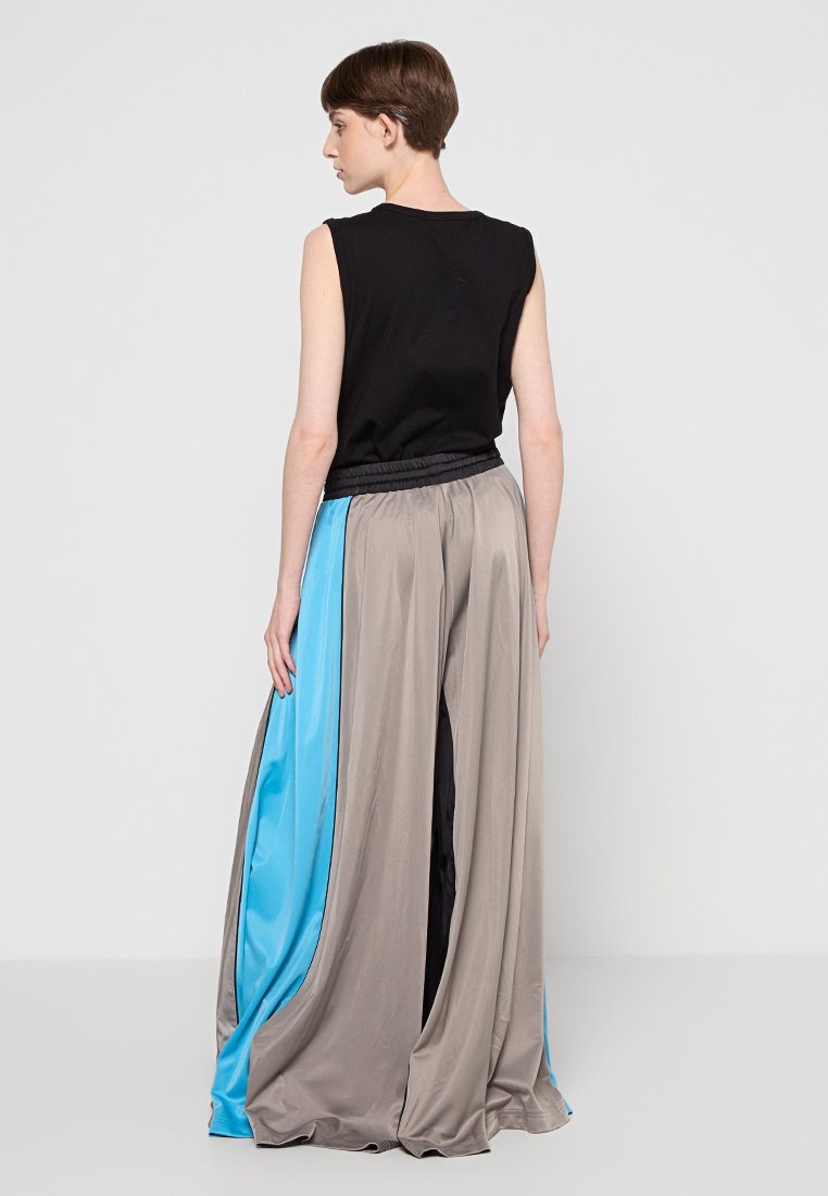 Un haut noir sans manches associé à un pantalon léger et ample avec des panneaux gris et bleus, une taille élastique et une texture fluide.