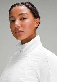 Veste blanche zippée avec un col haut, présentant une texture matelassée et des panneaux lisses, conçue pour un look ajusté.