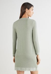 Světle zelené šaty s dlouhými rukávy, krajkovým lemem na spodním okraji a rukávech, vyrobené z jemné tkaniny, se jednoduchým a uvolněným střihem.