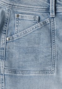 Jean en denim bleu clair avec une poche avant visible, des bords finis et des rivets en métal. Le tissu a une apparence texturée et usée.