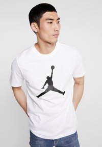 Hvid bomulds-T-shirt med et stort sort silhuettryk af en basketballspiller, der hopper med bolden. Kortærmet og med rund halsudskæring.