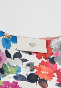 Květinová kabelka s bílou strukturovanou tkaninou a zářivými multicolor květinami. Obsahuje malou kovovou logo na bílém poli.