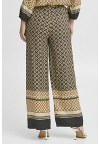 Pantalons évasés en tissu foncé avec un motif géométrique. Présente des bandes à motif de couleur claire au niveau de l'ourlet et une texture fluide.