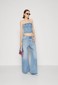 Top bustier en denim et jeans à jambes larges en bleu clair. Accentué par un petit sac à main rose et des lunettes de soleil noires. Texture lisse, design décontracté.