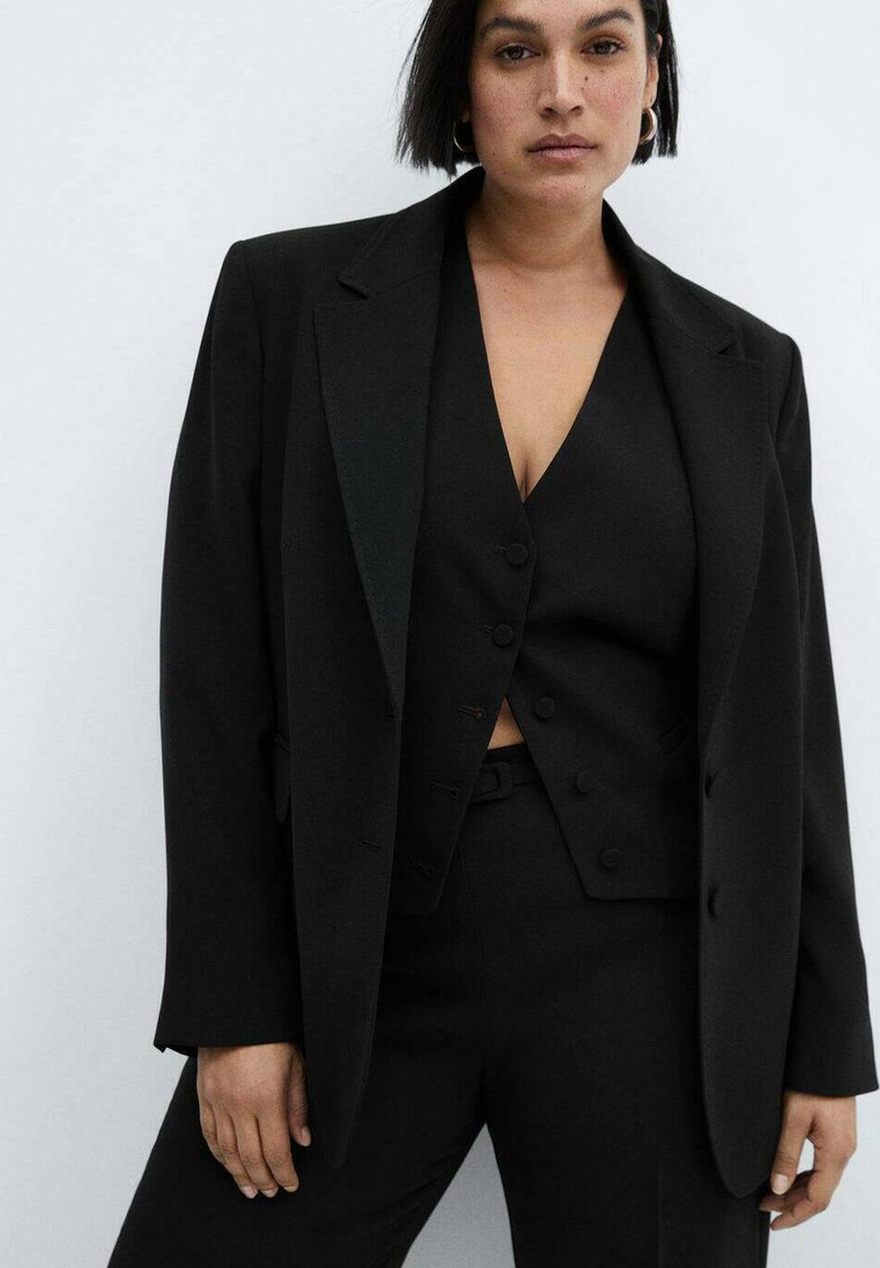 Schwarzer maßgeschneiderter Anzug mit einem prägnanten Blazer, taillierter Weste mit Knöpfen und passenden Hosen; der Stoff hat eine glatte Textur.