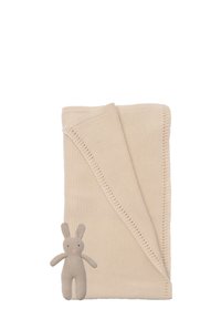 Beige gestrickte Decke mit gefaltetem Rand, kombiniert mit einem kleinen beigen Kaninchen-Spielzeug, das gestickte Gesichtsdetails und Ohren hat.