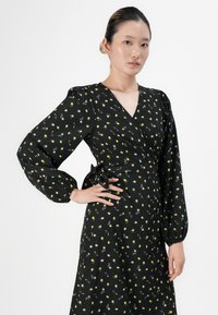 Black wrap dress with long puff sleeves, featuring a floral pattern in yellow and green. Textured fabric with a tied waist detail.