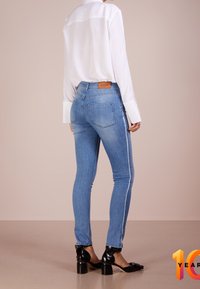 Höga blå denimjeans med smal passform, vita sidostrecker och en brun läderlogotyp på midjebandet.