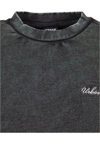 Sweat-shirt à col ras du cou gris foncé avec « Urban » brodé en lettres cursives blanches sur le haut du côté gauche de la poitrine.