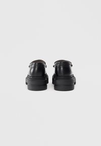 Zwarte leren schoenen met een ronde neus, dikke zool en een minimalistisch ontwerp. Voorzien van stiksels en een gegraveerd merk op de hak.