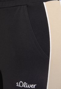 Schwarze Sporthosen haben ein seitliches Panel in Beige und einen dezenten weißen Akzent entlang der Naht. Der Stoff ist glatt und hat eine klassische Passform.