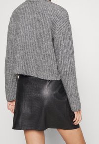 Szary sweter wykonany na drutach o skróconym fasonie, w połączeniu z czarną skórzaną mini spódnicą o fakturze wytłoczonego krokodyla.