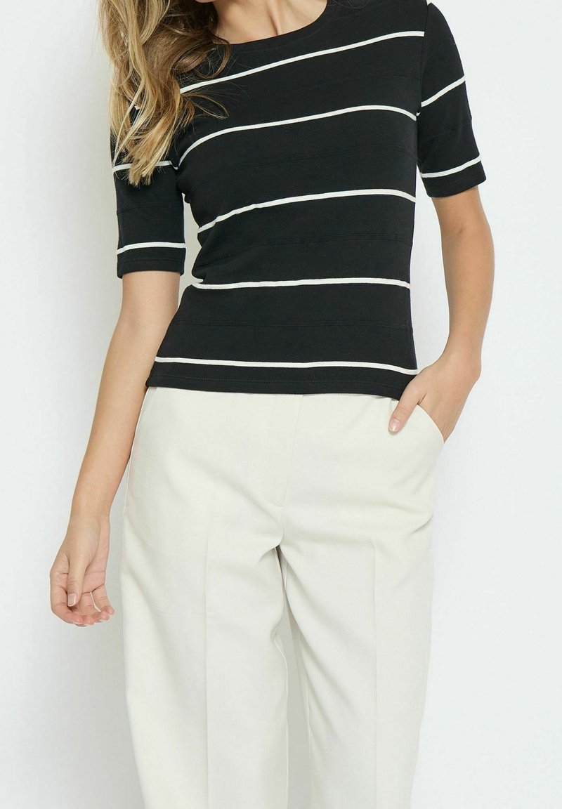 Haut à rayures noires avec rayures horizontales blanches, manches courtes, encolure ronde et tissu texturé ; associé à un pantalon beige clair.