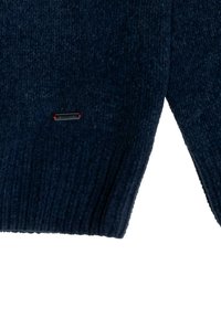 Granatowy sweter z dzianiny o prążkowanej fakturze, z małym czarno-czerwonym logo na dole. Rękawy delikatnie zwężają się ku mankietom.
