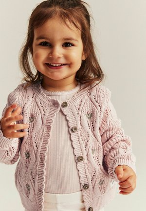 Jasnoróżowy dziergany kardigan z fakturowanym wzorem liści, okrągłym dekoltem i zapięciami na guziki, noszony na prążkowanym topie.