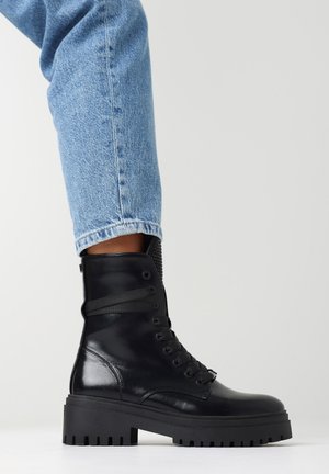 Zwarte leren enkellaarzen met een stevige zwarte zool, vetersluiting aan de voorkant en een gestructureerd rugpaneel. Draag ze met opgerolde lichtblauwe jeans.