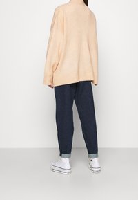 Light peach oversized sweater with ribbed hem, paired with dark blue tapered jeans and white high-top sneakers. Simple, soft texture.