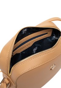Interno di una borsa in pelle testurizzata color beige, con due tasche a scomparsa e una fodera nera caratterizzata da un motivo a logo ripetuto. Dettaglio con zip dorata.