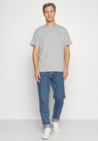 Siva bombažna majica s kratkimi rokavi, okroglim izrezom in majhnim logotipom na prsih, kombinirana s svetlo modrimi džins hlačami in belimi supergami.