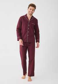 Burgundské pyžamo obsahující košili s knoflíky a kapsou na prsou, s bílým lemem, doplněné o odpovídající kalhoty se rovnými nohavicemi. Vyrobeno z jemné látky.