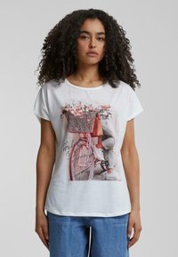 T-shirt blanc à manches courtes avec un design imprimé d'un vélo rose avec un panier fleuri et le texte "le meilleur est à venir."