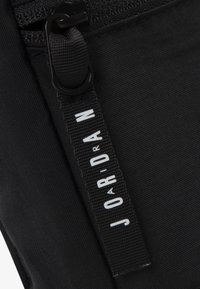 Svart tygdragkedjepåse med en strukturerad yta, med en framträdande etikett med "JOARDAN" i fet stil vita bokstäver.