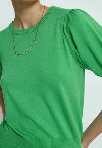 Grüner Strickpullover mit kurzen Puffärmeln, geripptem Ausschnitt und Saum. Hergestellt aus weichem Stoff, mit glatter Textur und figurnahem Design.