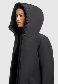 Must värviline kapuutsiga jakk, millel on sile, mati tekstuur; sisaldab lukuga sulgemist, suurt kapuutsi ja külgtaskuid. Aktsent on varrukal olev logoga.