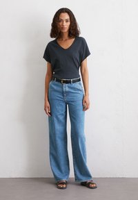 Top grigio con scollo a V e maniche corte abbinato a jeans di denim blu a gamba larga, fissato con una cintura nera con fibbia dorata. Sandali neri piatti.