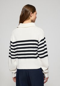 Cropped sweater in cream with black horizontal stripes. Features a folded collar and slightly puffed sleeves. Soft knit texture.