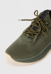 Botte de sport vert olive avec un dessus en tricot texturé, design à lacets, semelle en caoutchouc et col rembourré pour le confort.