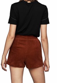 Donna che indossa un top corto nero con borchie argentate e pantaloni corti in corduroy color ruggine a vita alta, mostrata da dietro.