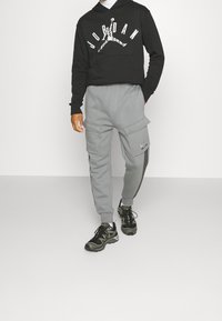 Czarna bluza z kapturem z białym logo "JORDAN", w połączeniu z szarymi spodniami dresowymi typu cargo z bocznymi kieszeniami i czarnymi akcentami, uzupełniona czarnymi butami.