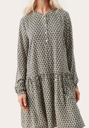 Mujer con vestido de manga larga con un patrón repetitivo en forma de abanico en blanco y negro y escote redondo con botones.