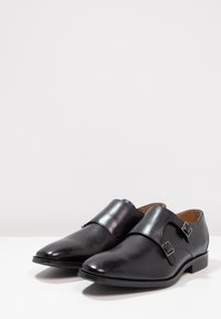 Chaussures habillées en cuir noir avec une finition polie, présentant un bout arrondi, des sangles à double boucle et un talon bas.