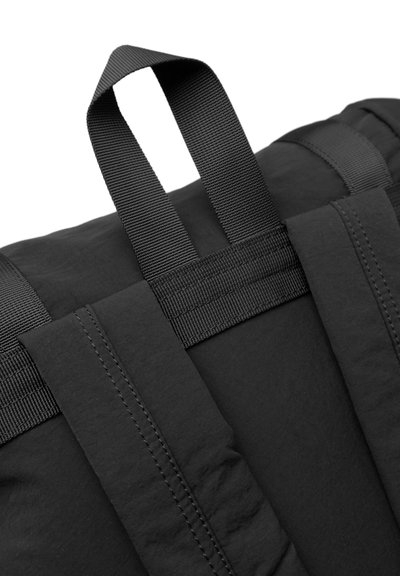 Sac noir en tissu texturé, doté de deux poignées robustes en tissu et de détails de couture visibles le long des bords.