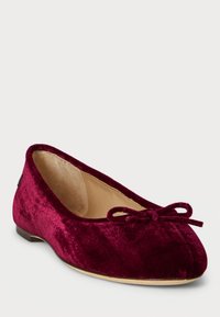 Samettinen burgundinpunainen ballerina kenkä, jossa on pieni nauha pyöreässä varpaassa ja beige sisävuori, valkoista taustaa vasten.