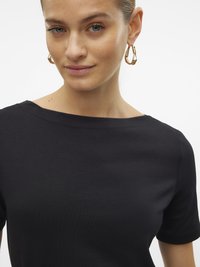 Čierny top s krátkym rukávom a okrúhlym výstrihom, vyrobený z hladkej tkaniny. Modelka nosí zlaté kruhové náušnice ako doplnok.