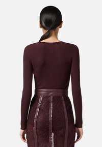 Maglietta bordeaux a maniche lunghe con scollo rotondo abbinata a una gonna di pizzo con dettagli in pelle e pannelli trasparenti.