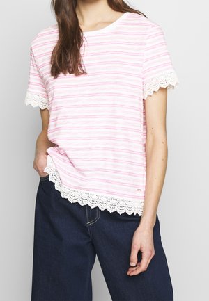 Femme portant un chemisier à manches courtes rayé rose et blanc avec une bordure en dentelle aux manches et à l'ourlet, associé à un jean bleu foncé.