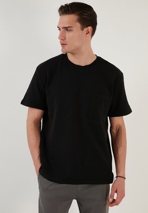 Sort kortærmet t-shirt lavet af tekstureret stof, med rund hals og en brystlomme på venstre side.