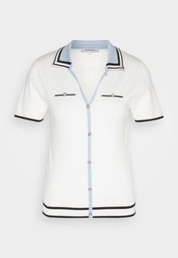 Haut polo à manches courtes blanc avec des accents bleu et noir, présentant un col en V, deux poches avant et une fermeture à boutons. Texture tricot lisse.