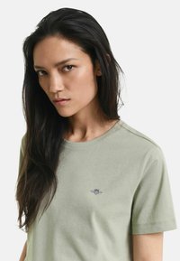 Olijfgroene katoenen t-shirt met een ronde hals, korte mouwen en een klein geborduurd logo op de borst. Zachte textuur met een minimalistisch ontwerp.