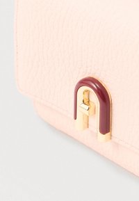 Artimiausias planas rodo rožinės tekstūruotos odos sklendę su auksiniu ir vynuogiškai raudonu U formos užsegimu ant rankinės.