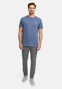 T-shirt azzurro chiaro a maniche corte con la scritta "JEFF" stampata sul petto, abbinato a pantaloni grigi slim-fit e sneakers grigie.